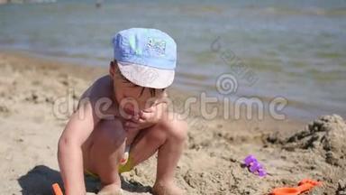 一个孩子在阳光明媚的热天在海滩上玩沙子和玩具